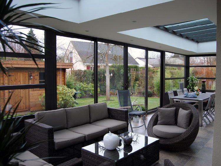 Véranda avec mobilier sombre, donnant sur une cour arrière avec table à manger et jardin.