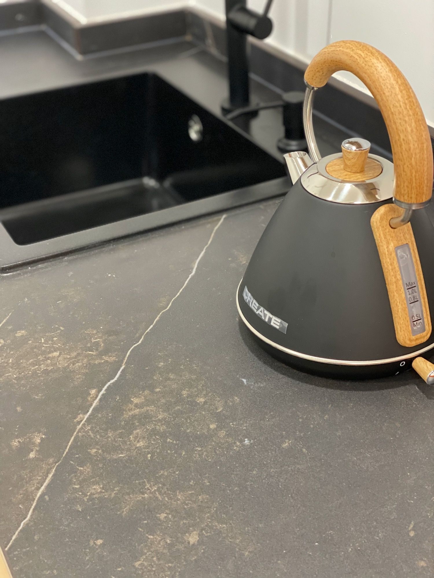 Hay una tetera negra sobre un mostrador al lado de un fregadero.