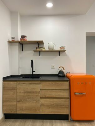 Una cocina con gabinetes de madera, un fregadero y un refrigerador naranja.