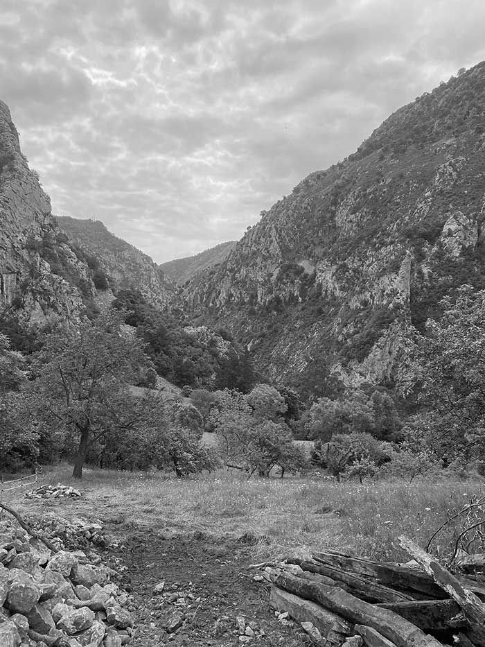 Un paisaje en blanco y negro que muestra un valle entre montañas escarpadas y rocosas bajo un cielo nublado y cubierto de nubes.