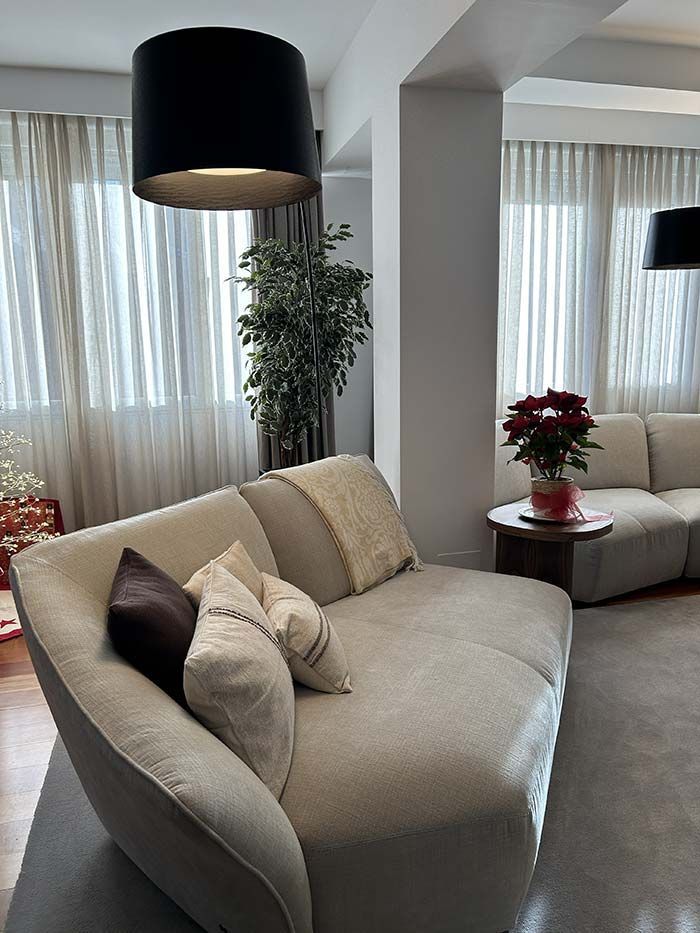 Un salón luminoso y moderno con un sofá mullido de color crema, una pequeña mesa auxiliar con una flor de Pascua y lámparas de pie.