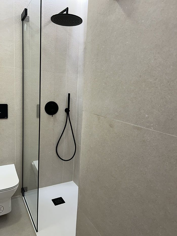 Una cabina de ducha moderna con una ducha de efecto lluvia de techo en negro mate, una alcachofa de ducha de mano a juego y una mampara de cristal.