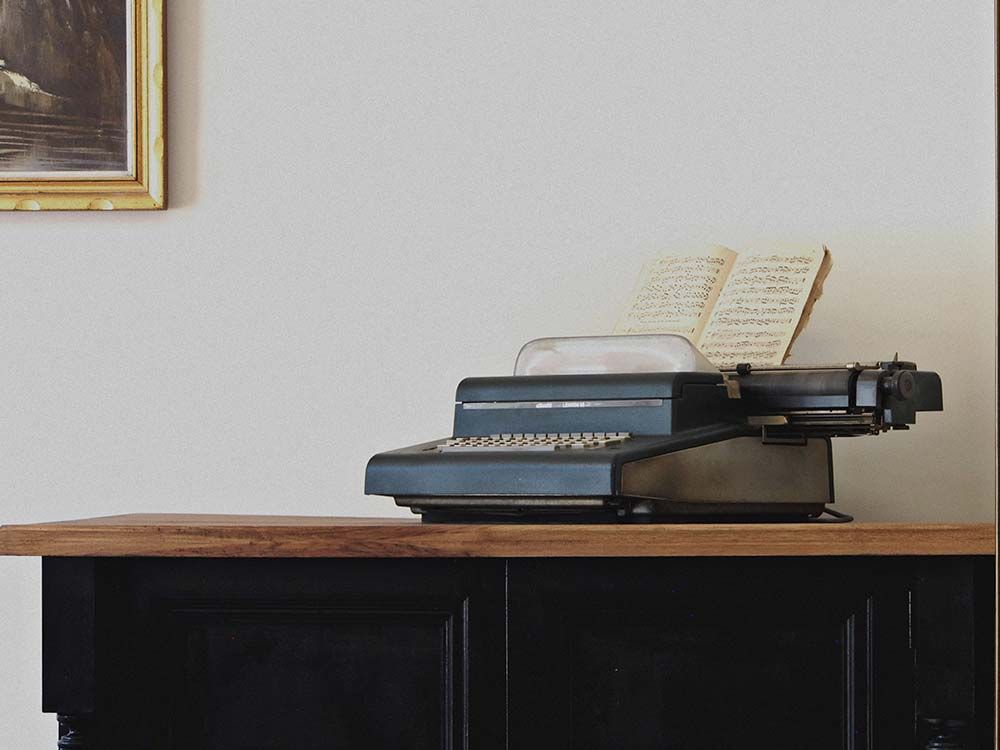 Una máquina de escribir negra antigua con una nota escrita a mano descansa sobre una superficie de madera oscura contra una pared lisa.