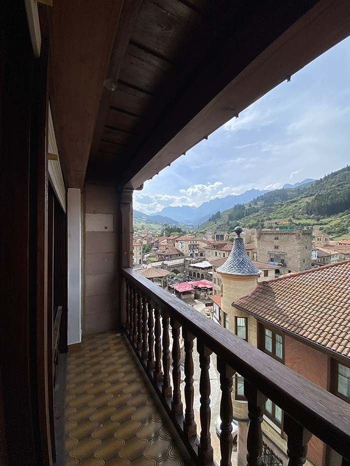 Vista desde un balcón de madera con vistas a un pueblo de estilo español enclavado en un valle con montañas al fondo.
