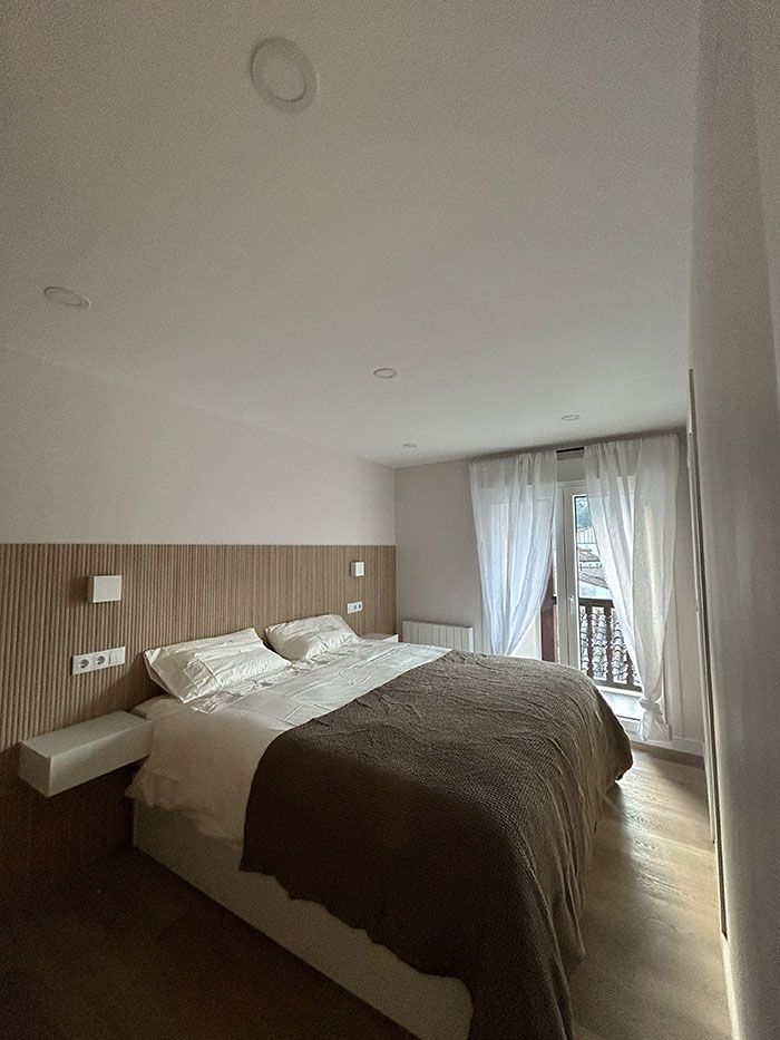 Un dormitorio con una cama doble con almohadas blancas y una manta texturizada marrón, colocada contra una pared con cabecero de madera.