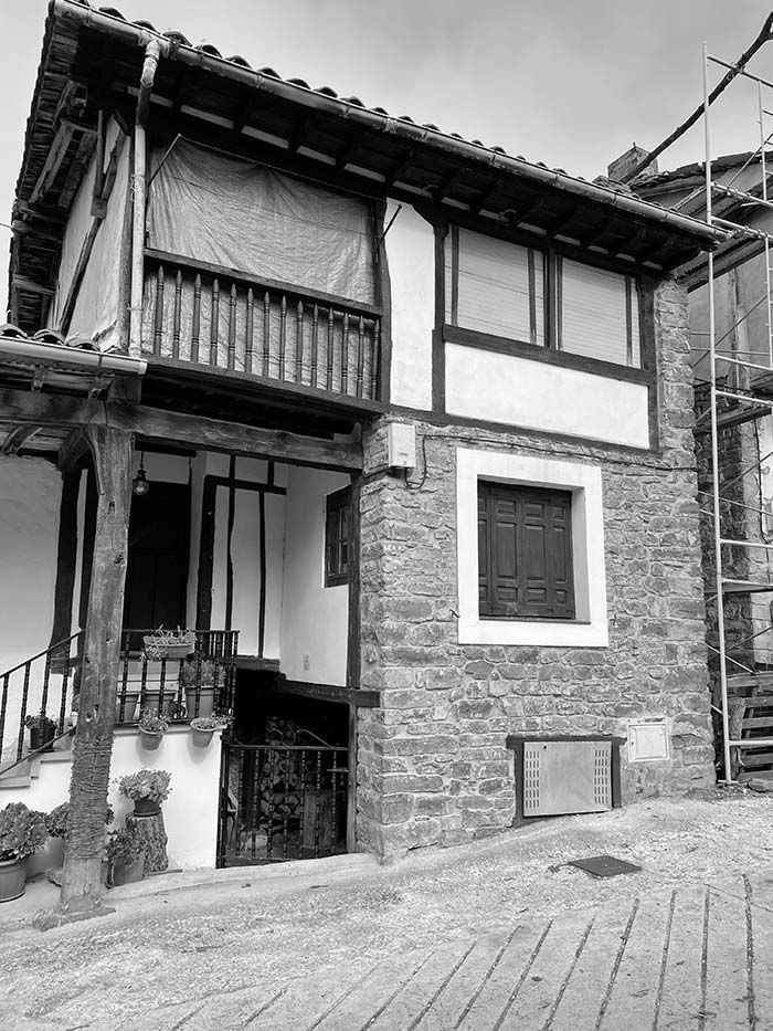 Una casa de dos plantas, construida en piedra y entramado de madera, con balcón y porche abierto a nivel de la calle, situada en una calle empedrada.