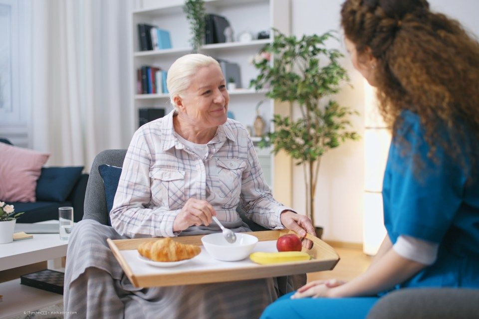 fairpflegt GbR – eine ältere Dame lächelt eine Pflegefachkraft an, während sie sich über ihr Frühstück freut