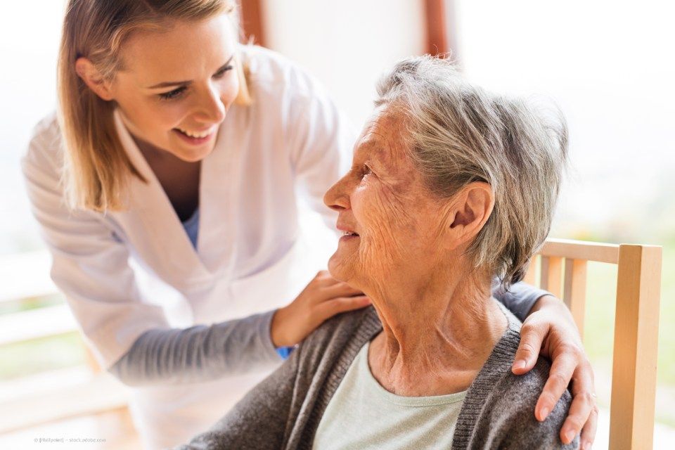 fairpflegt GbR – eine Pflegerin beugt sich lächelnd über eine sitzende, ältere Dame