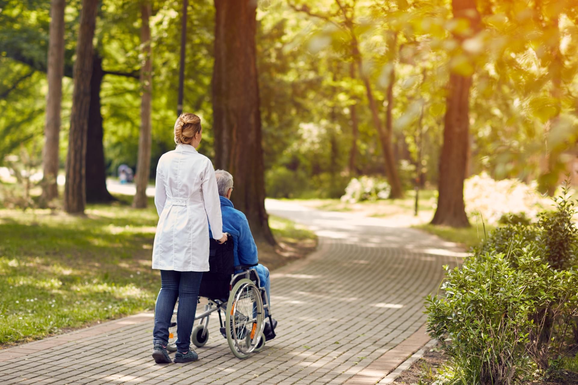 fairpflegt GbR – eine Frau in weißer Jacke und ein Mann im Rollstuhl gehen gemeinsam durch einen Wald