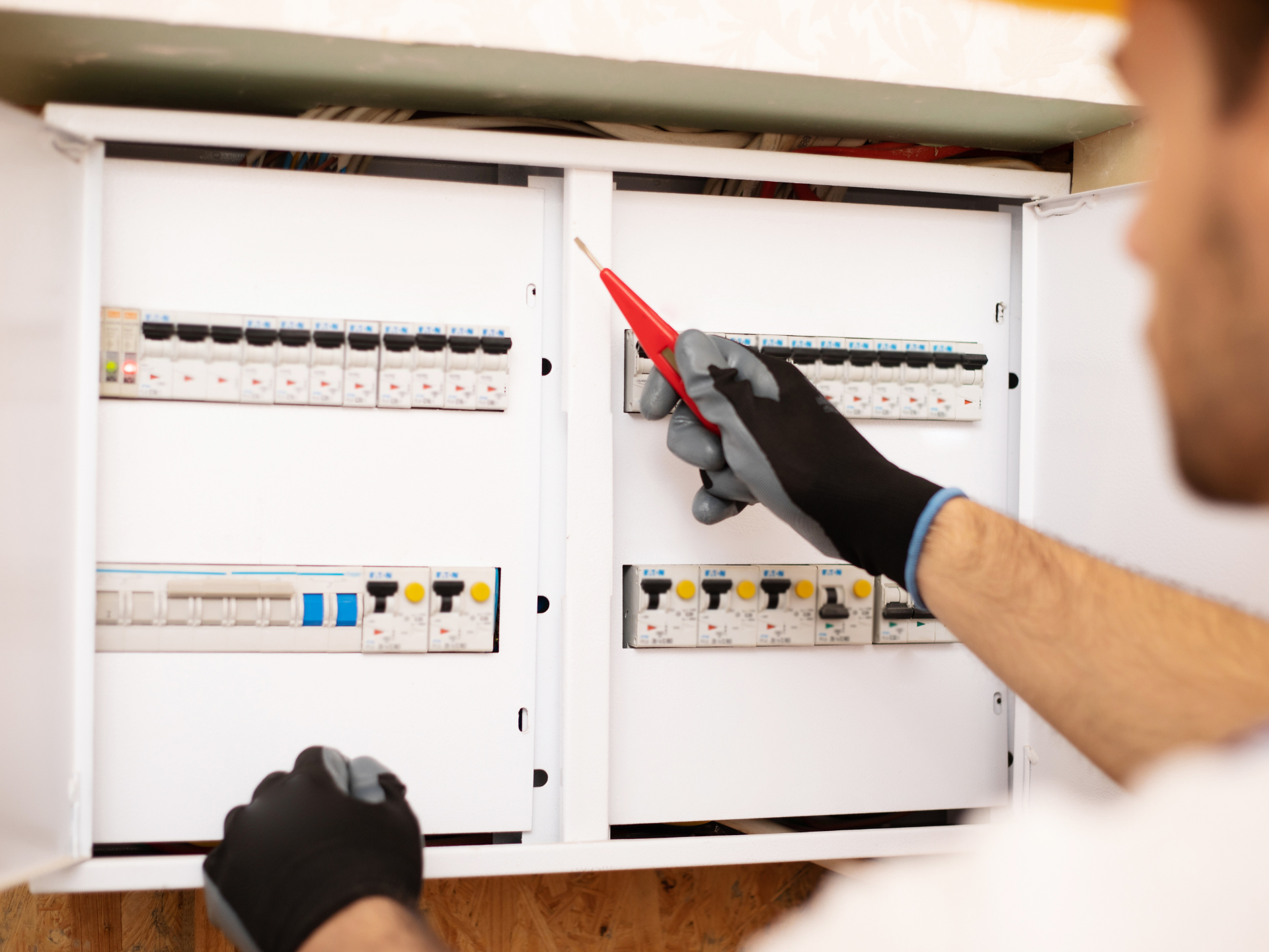 Électricien utilisant un testeur de tension sur un tableau électrique ; portant des gants.