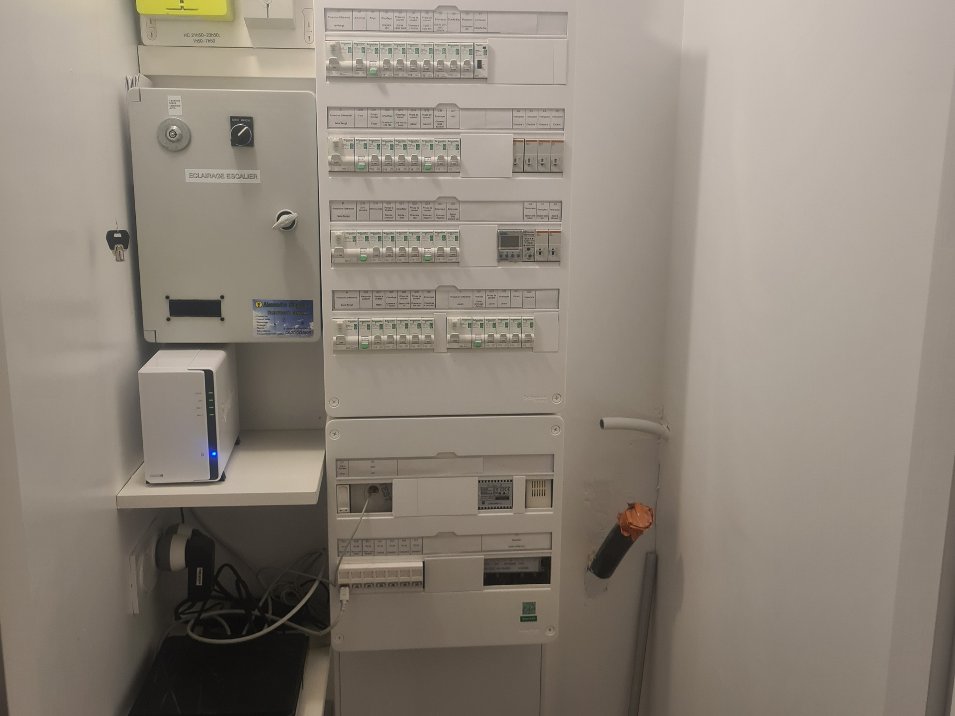 Tableau électrique et boîtier de commande blancs dans une armoire blanche, avec un dispositif réseau sur une étagère.