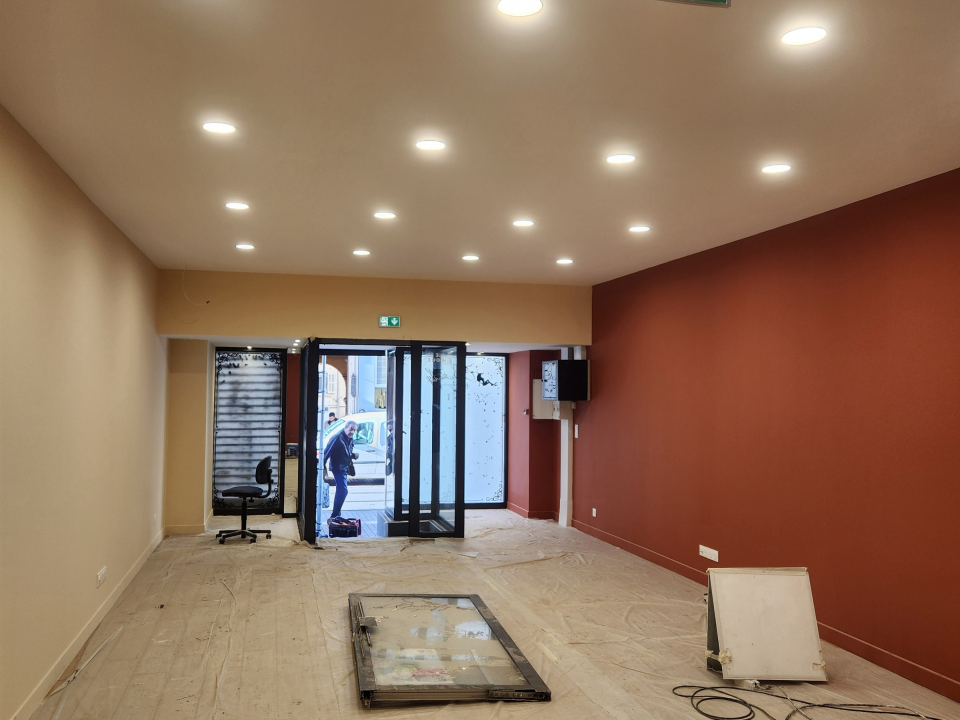 Pièce intérieure vide avec éclairage encastré, murs rouges et beiges, porte ouverte, débris de construction.