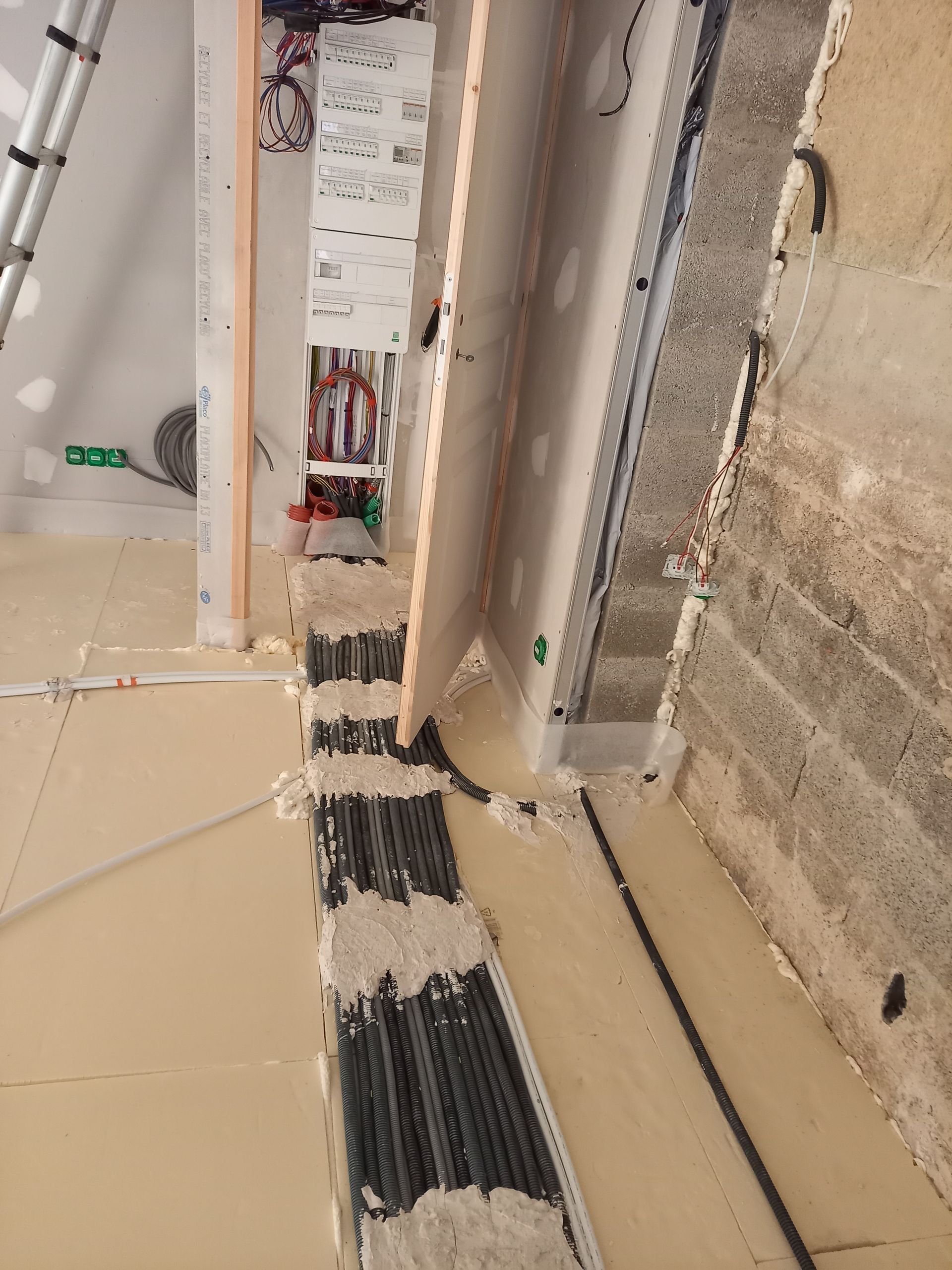 Chantier : Des câbles et des conduits électriques sont en cours d'installation dans un espace partiellement aménagé.