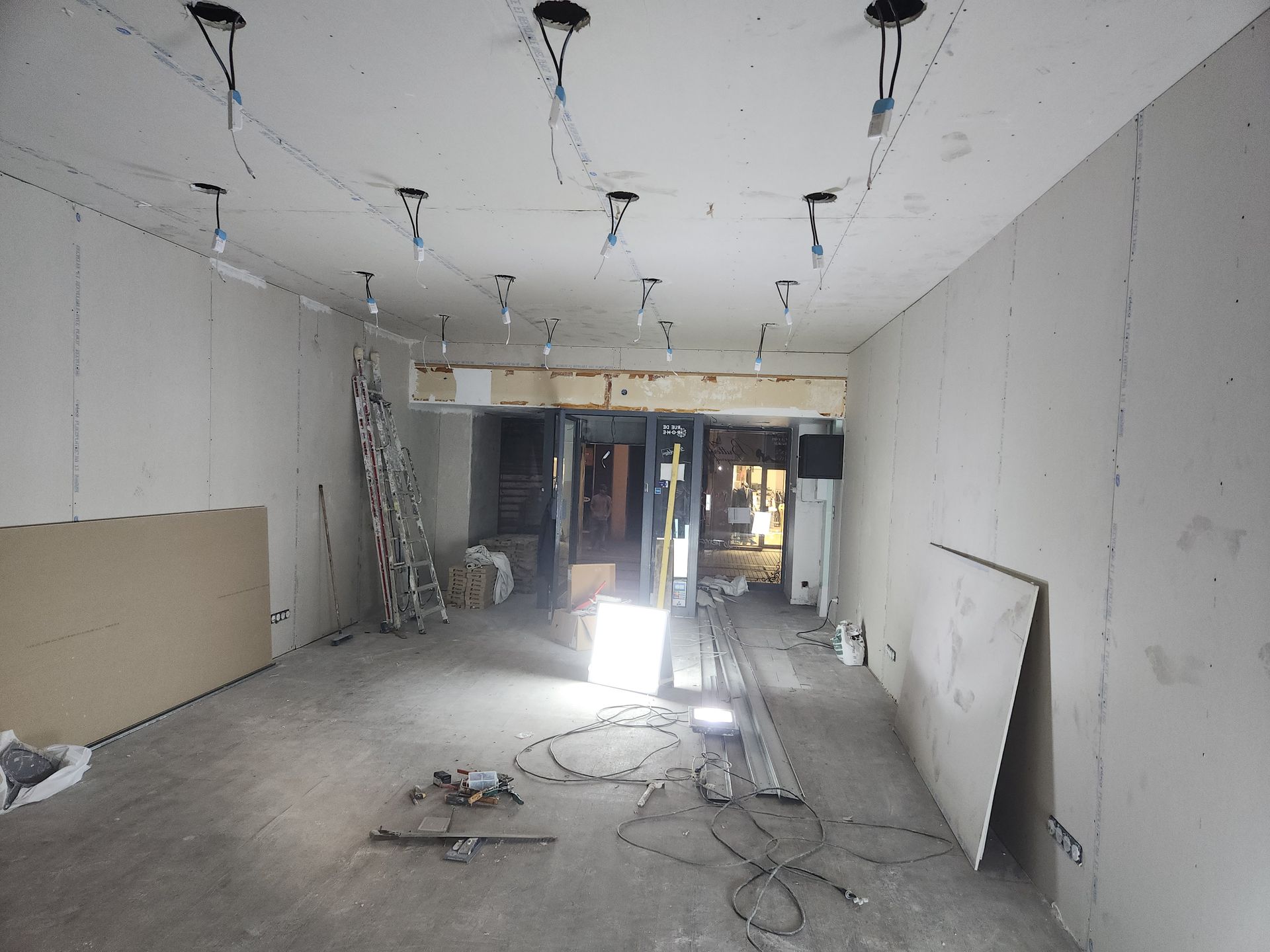 Intérieur en travaux, murs inachevés, plafond avec câblage, outils, porte ouverte.