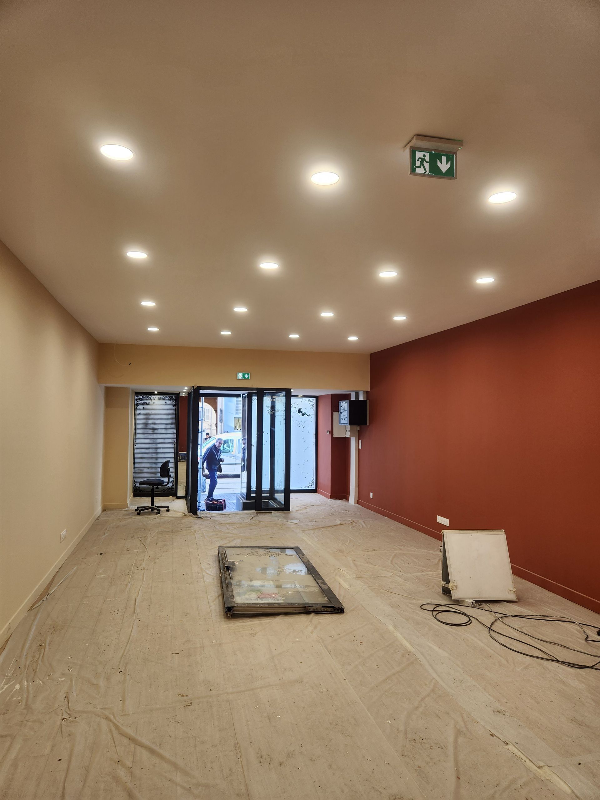 Une pièce vide aux murs beiges, un mur d'accent rouge, des spots encastrés et une personne près de l'entrée.