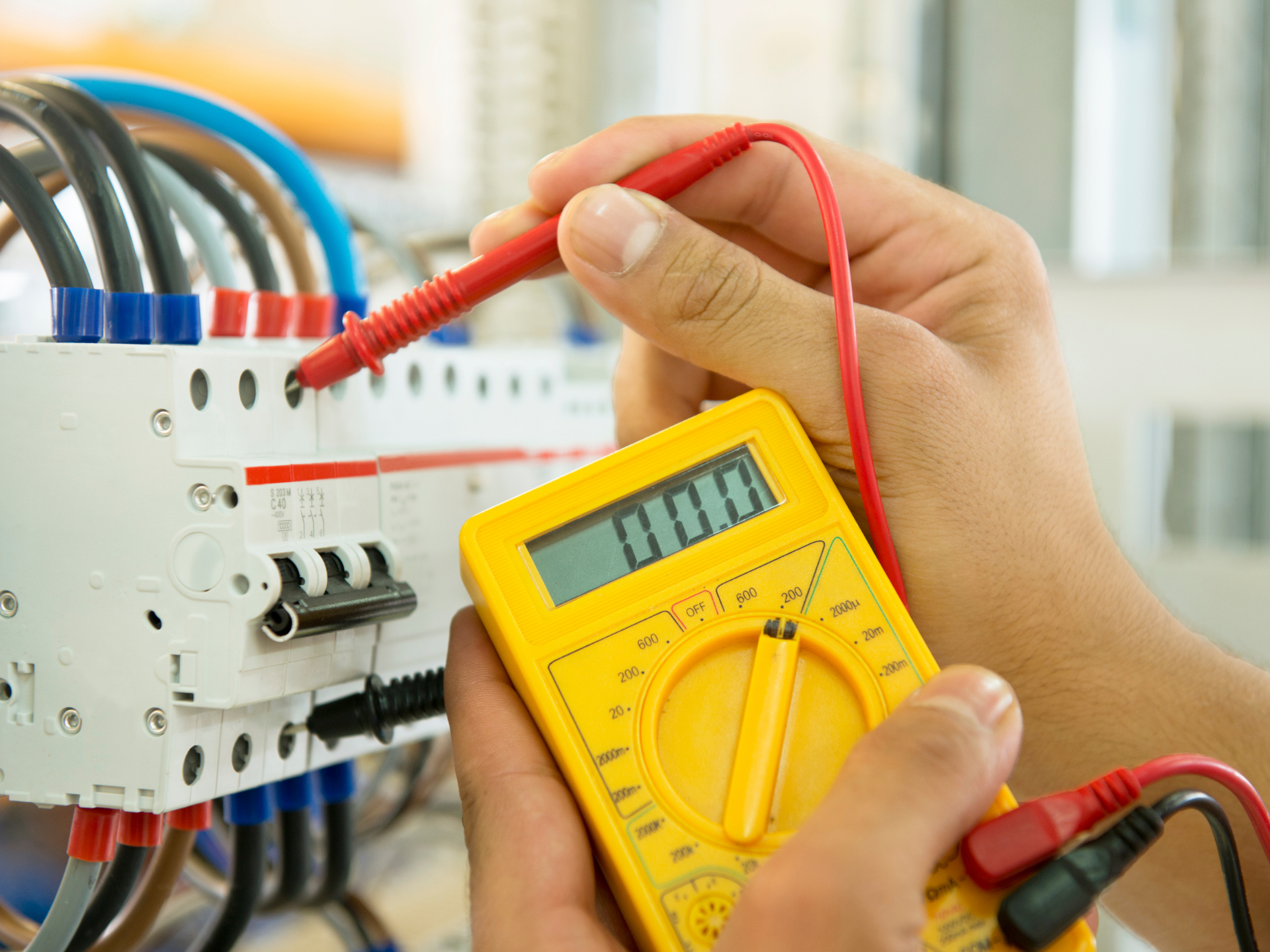 Un électricien utilise un multimètre pour tester un tableau de disjoncteurs ; sondes rouge et noire.