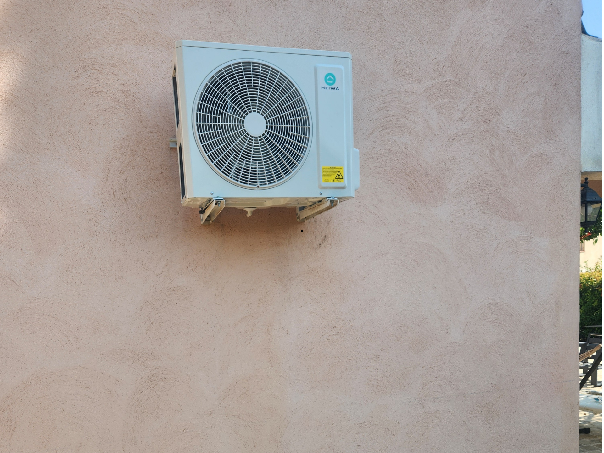 Unité de climatisation fixée sur un mur en stuc couleur pêche.