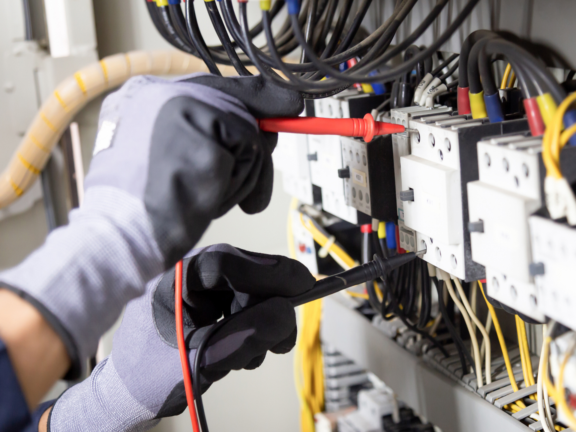 Un électricien ganté teste les fils à l'aide d'un multimètre dans un panneau de commande.