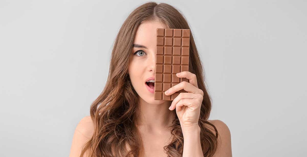 Una mujer sostiene una barra de chocolate frente a su cara.