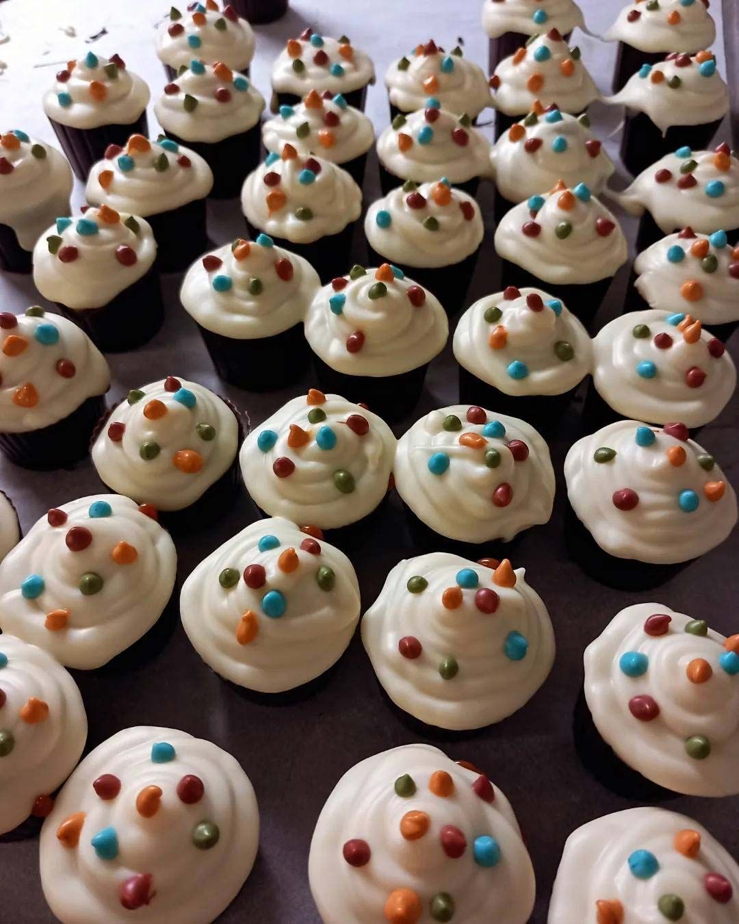 Un montón de cupcakes con glaseado blanco y chispas de colores.