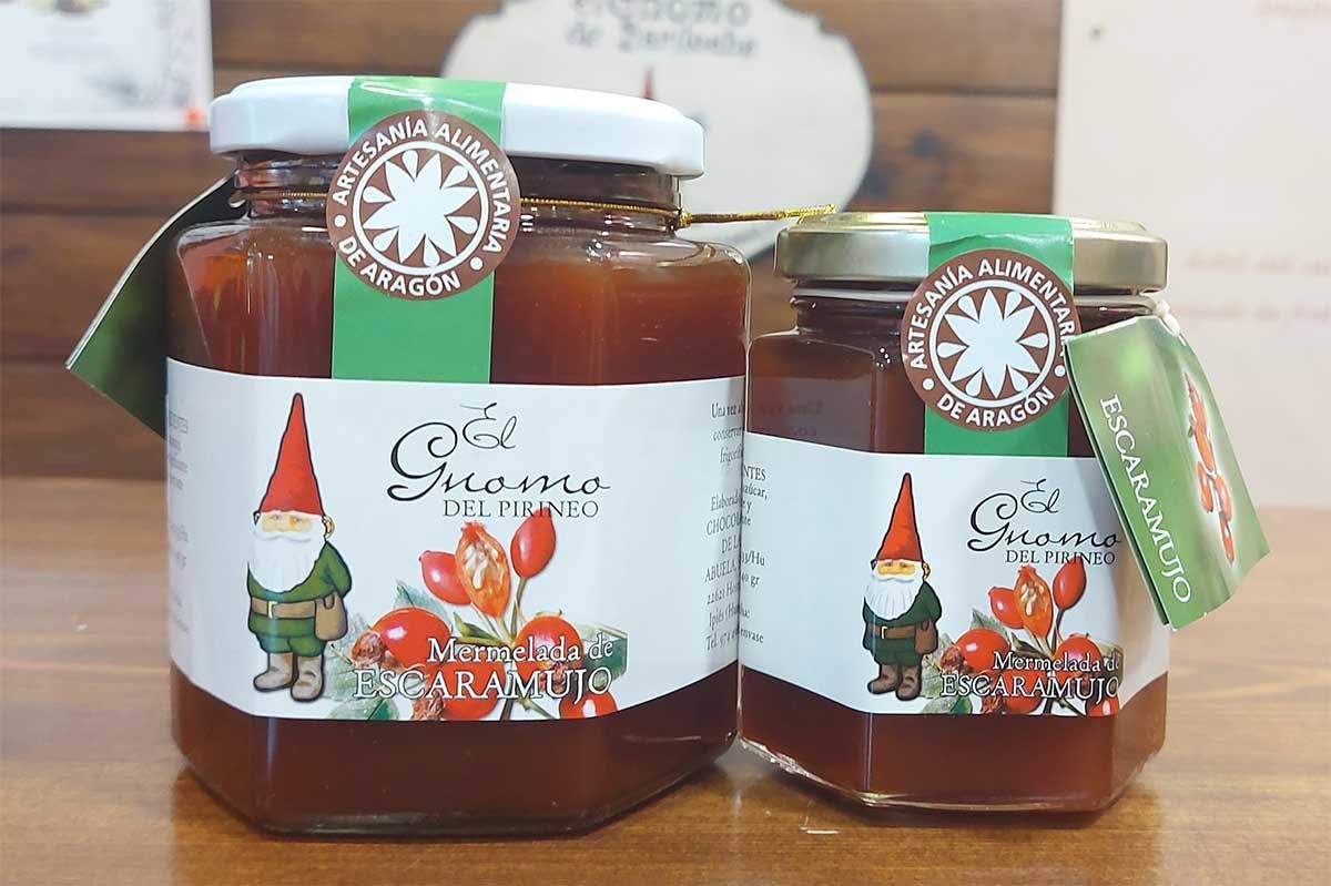 Dos frascos de mermelada con gnomos encima están sobre una mesa de madera.