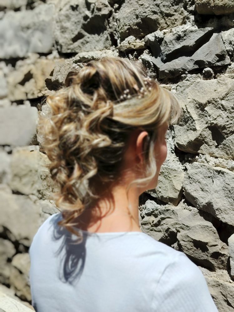 Femme avec une coiffure blonde relevée, debout devant un mur de pierre.