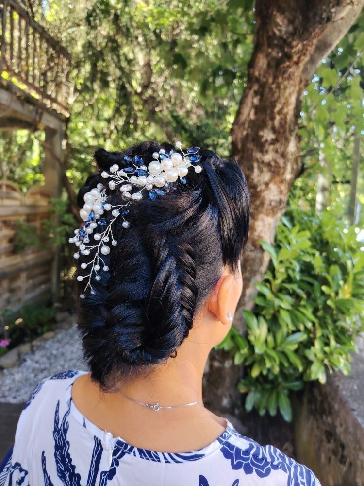 Femme aux cheveux foncés coiffés en chignon tressé, ornée d'un postiche floral blanc et bleu ; à l'extérieur.