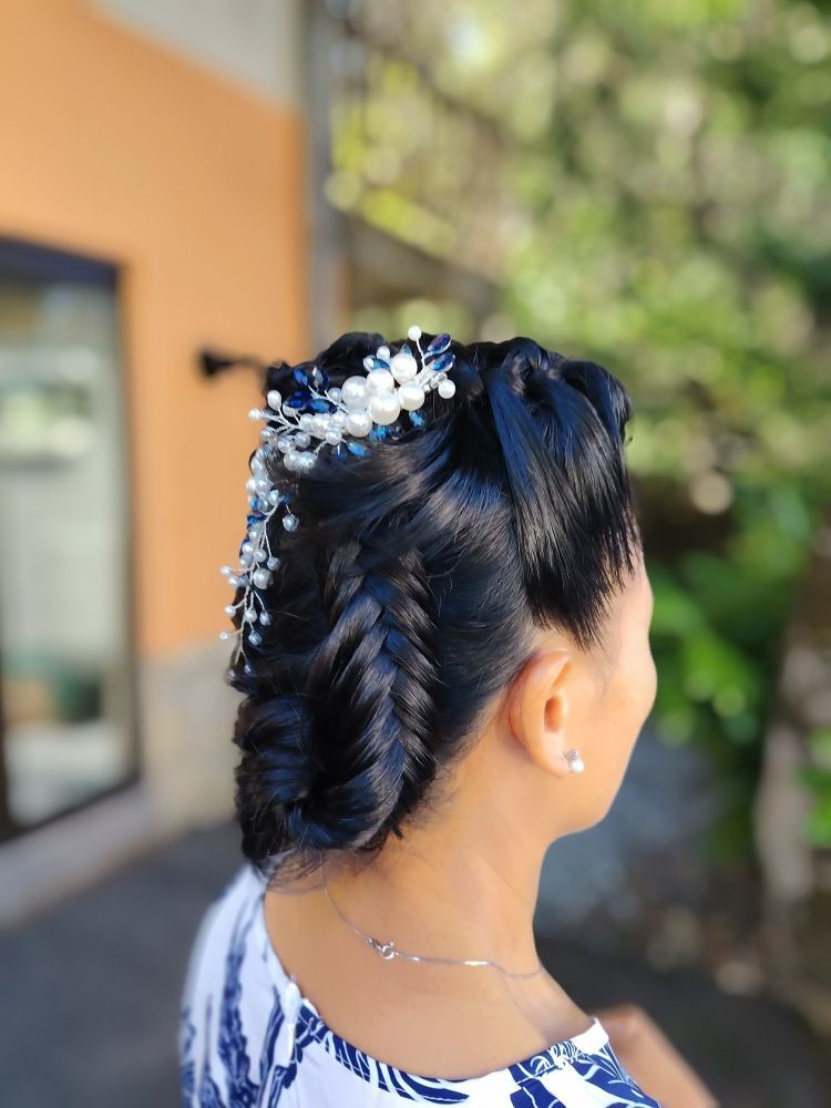 Femme aux cheveux noirs coiffés en tresse et chignon élaborés, ornés d'épingles à cheveux en perles, à l'extérieur.