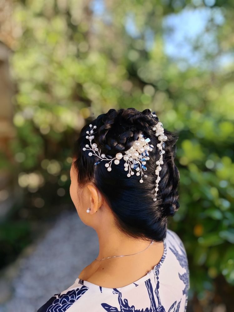 Femme aux cheveux noirs dans un chignon orné d'accessoires pour cheveux ornés de bijoux blancs et bleus, à l'extérieur.