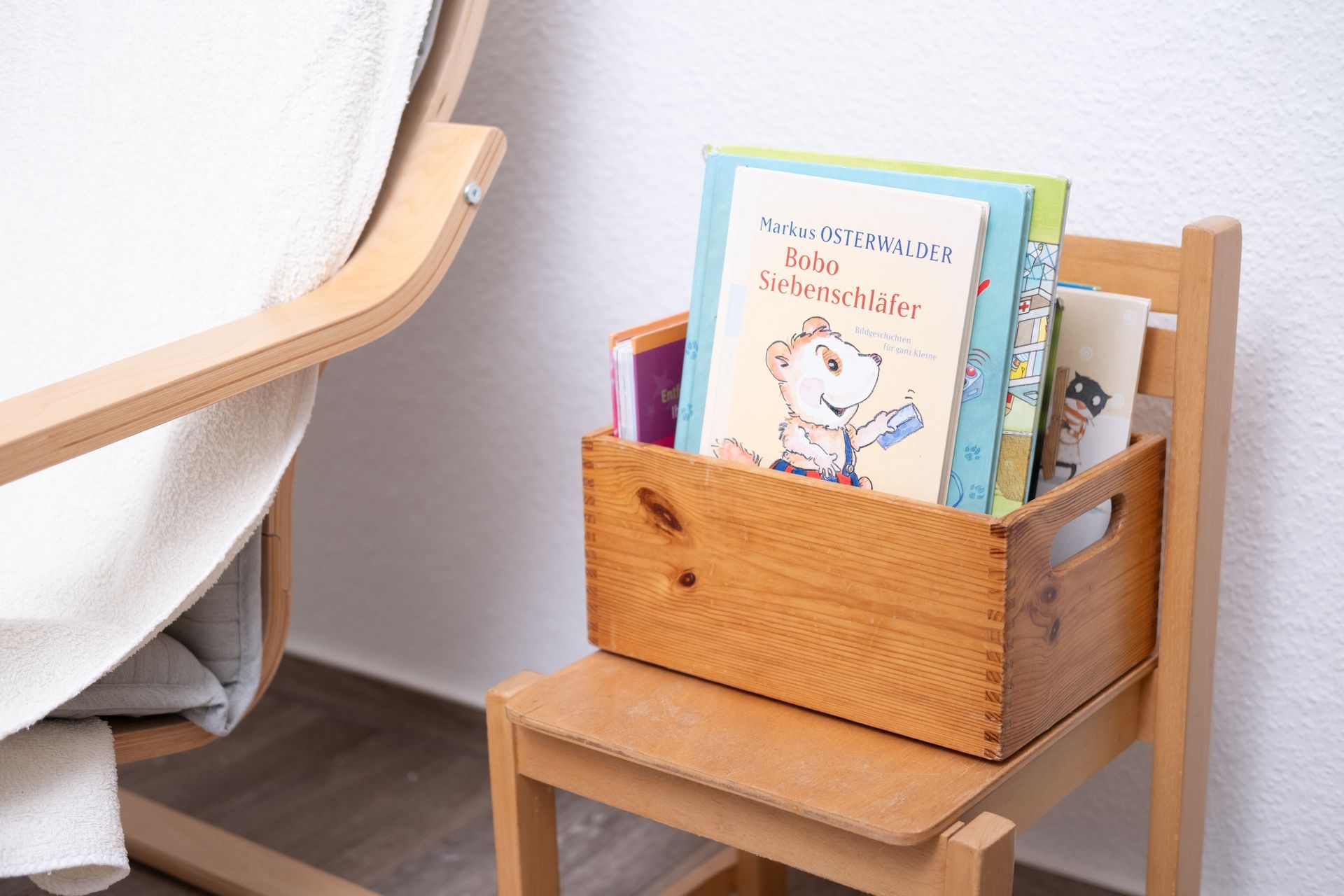 Auf einem Holzstuhl steht eine Holzkiste voller Bücher.