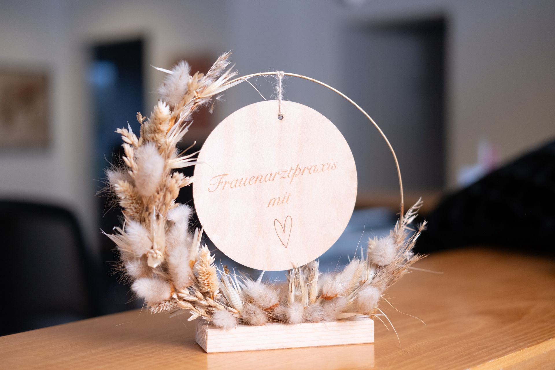 Auf einem Holztisch steht ein Holzschild mit getrockneten Blumen.