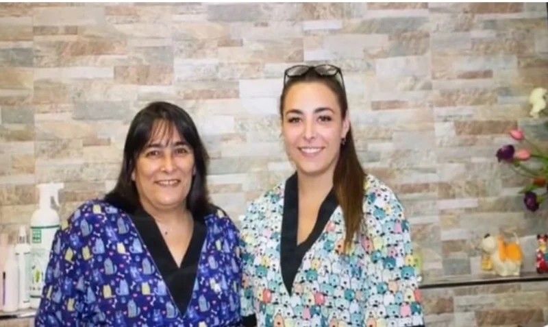 Dos mujeres sonrientes con blusas estampadas delante de un muro de piedra.