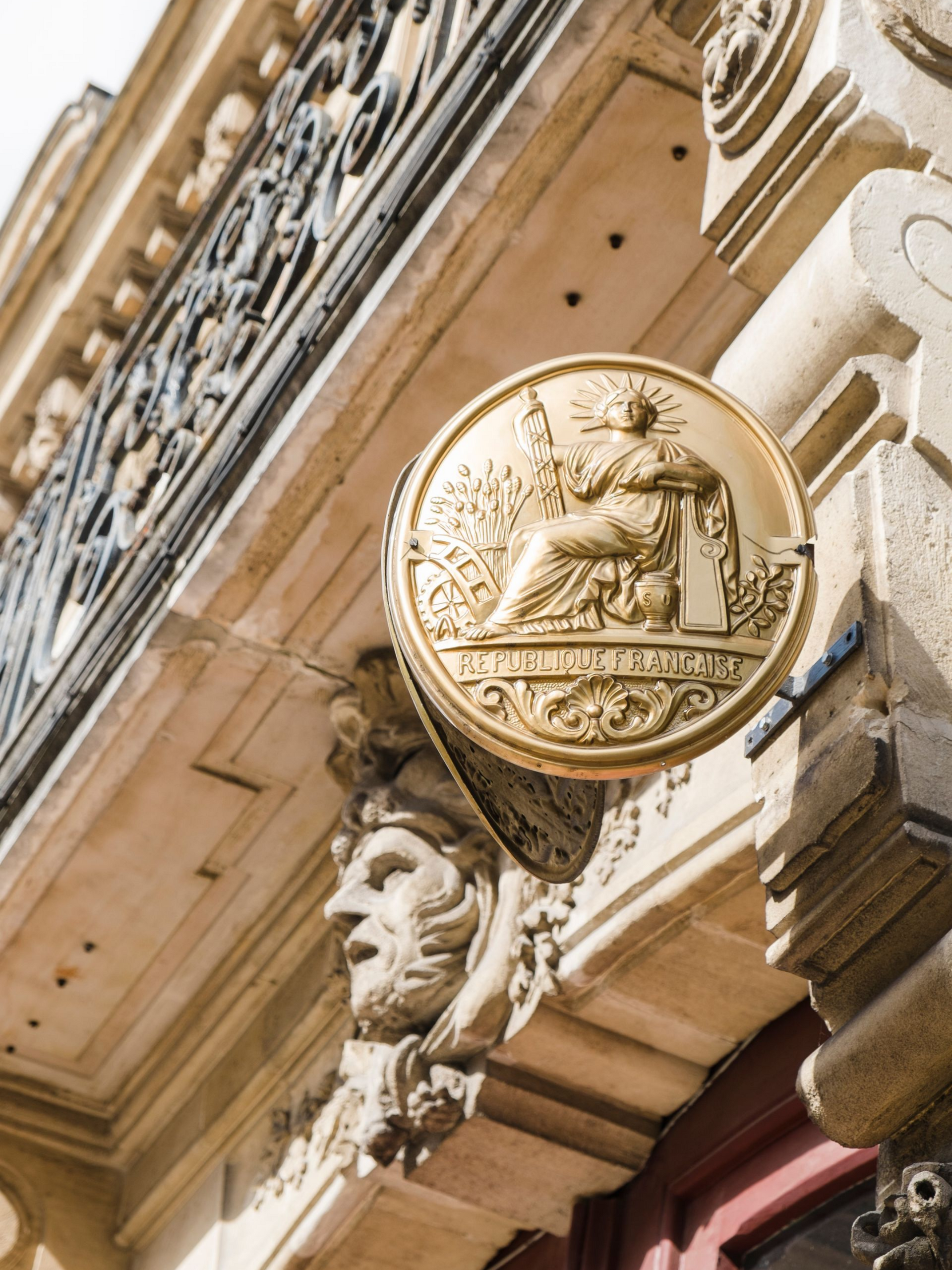Médaillon circulaire doré sur une façade en pierre.