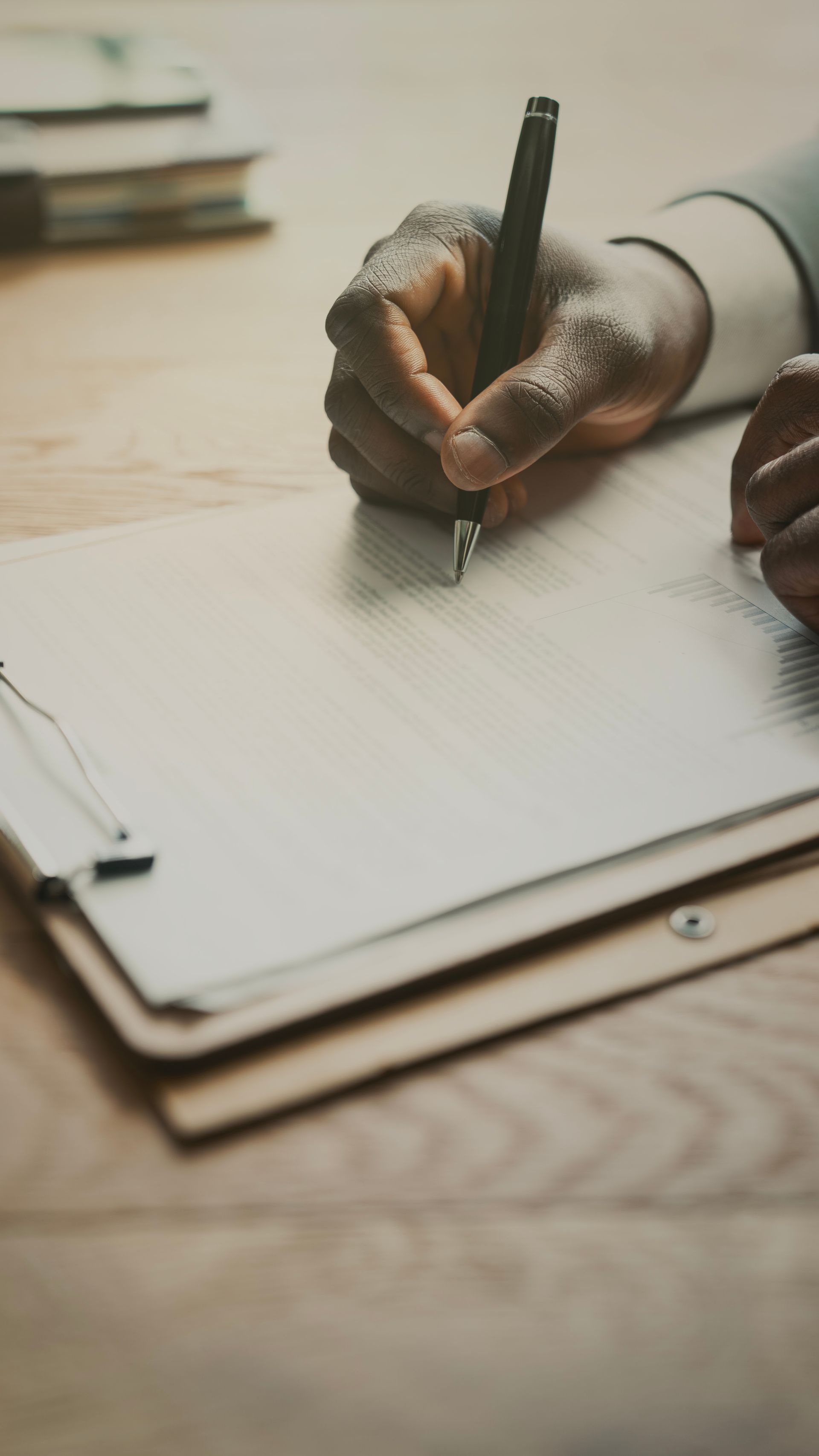 Écriture manuscrite sur un bloc-notes ligné avec un stylo noir à un bureau en bois.