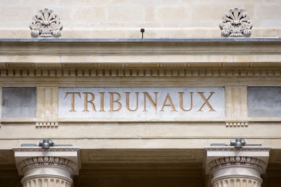 Façade en pierre d'un bâtiment avec l'inscription TRIBUNAUX au-dessus de colonnes et de sculptures ornementales.