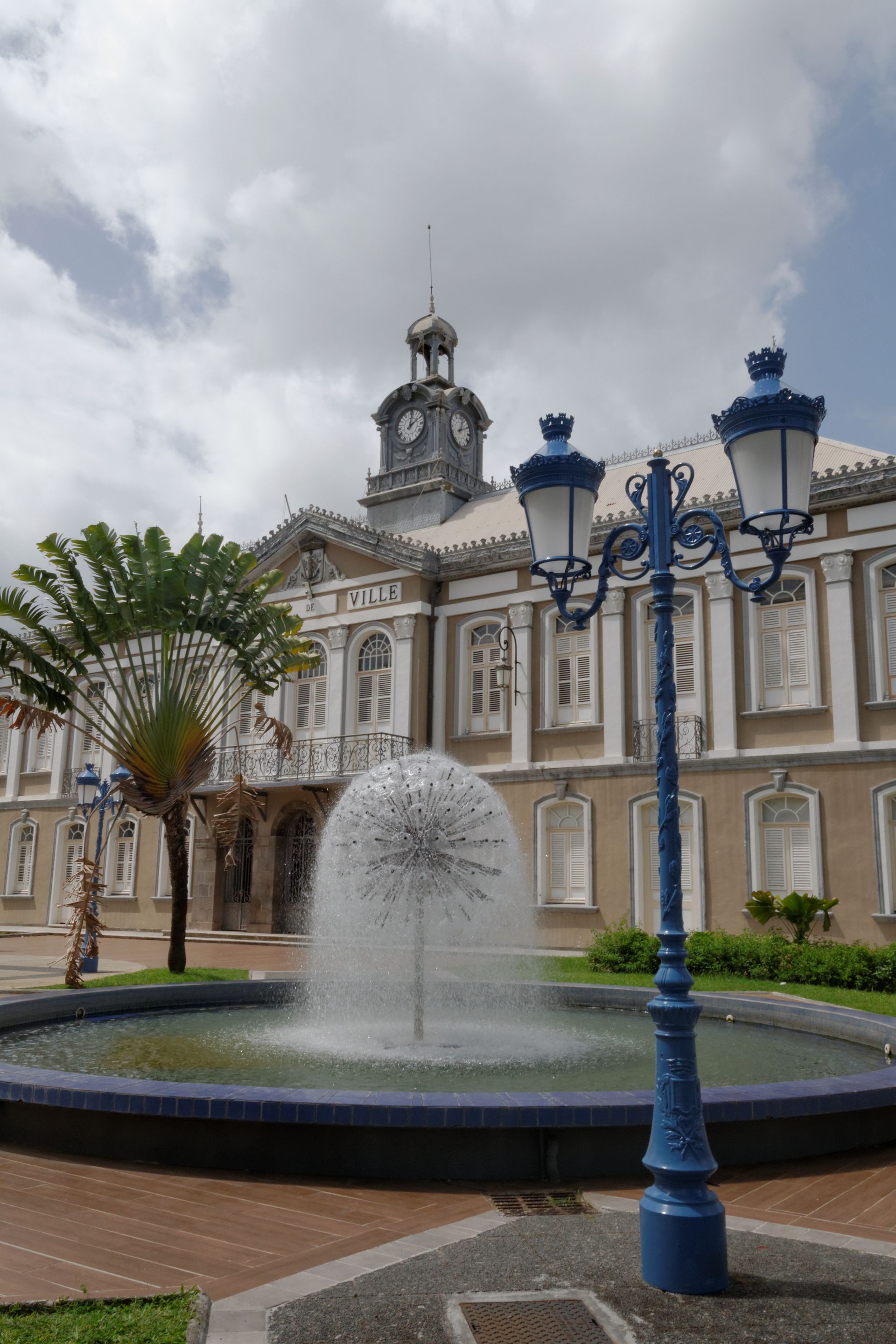 Bâtiment historique avec fontaine ornée et lampadaire bleu.