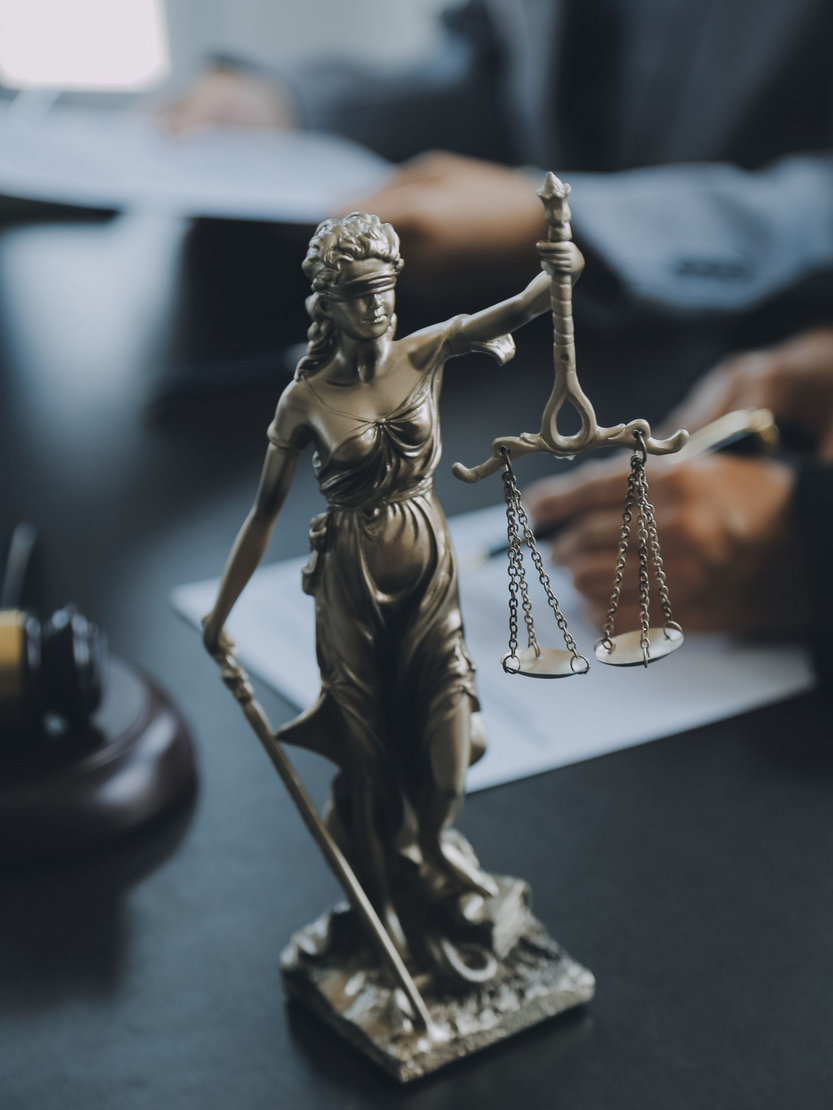 Statue de la Justice en bronze avec balance sur un bureau et des personnes en arrière-plan.