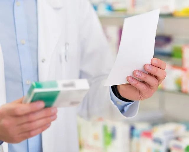 Un farmacéutico sostiene una caja de pastillas y un trozo de papel.