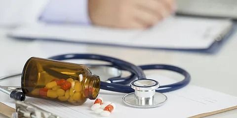 Sobre una mesa hay un frasco de pastillas, un estetoscopio y un portapapeles.