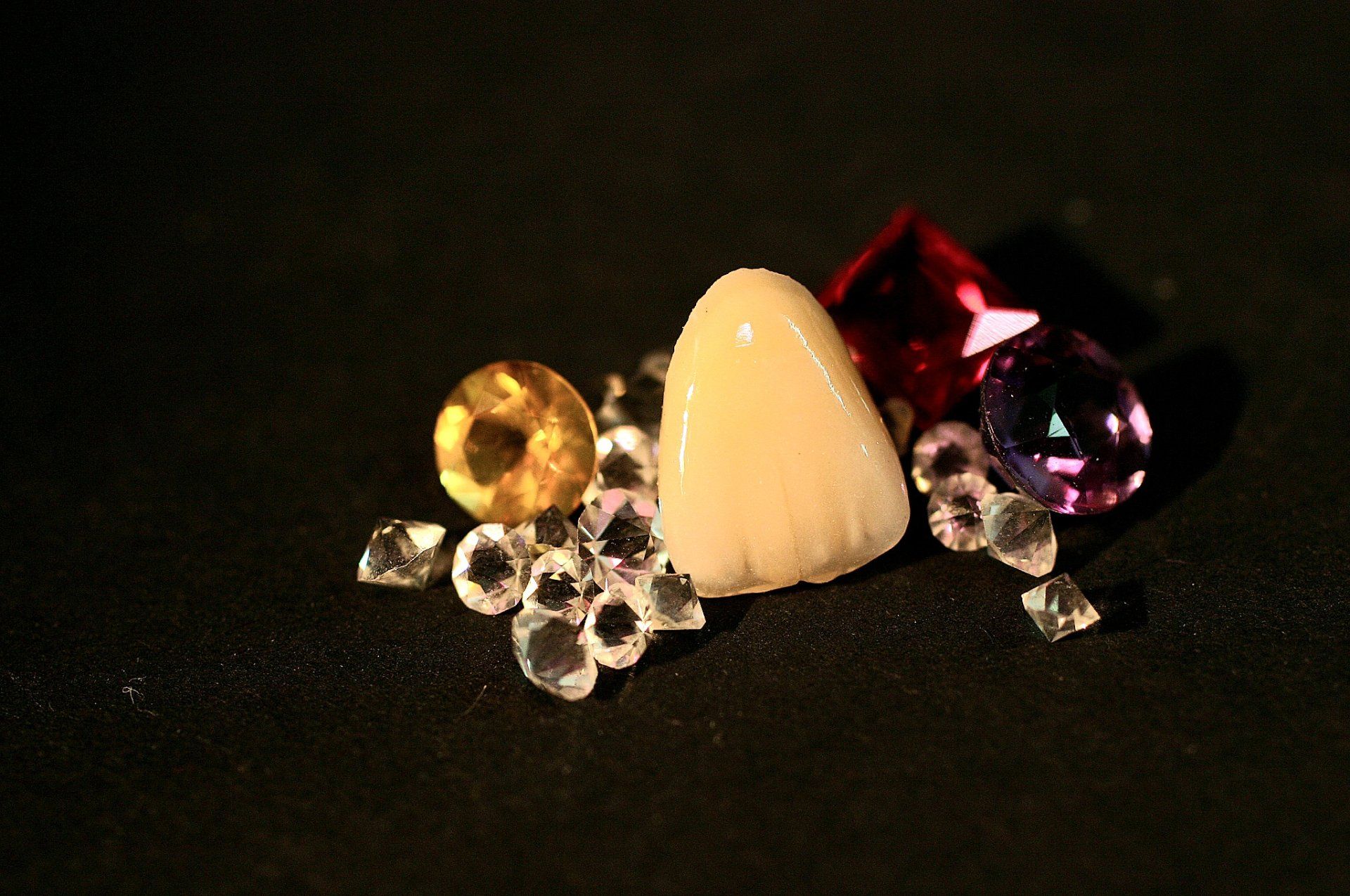 Ein Haufen Diamanten und ein Zahn auf einer schwarzen Oberfläche