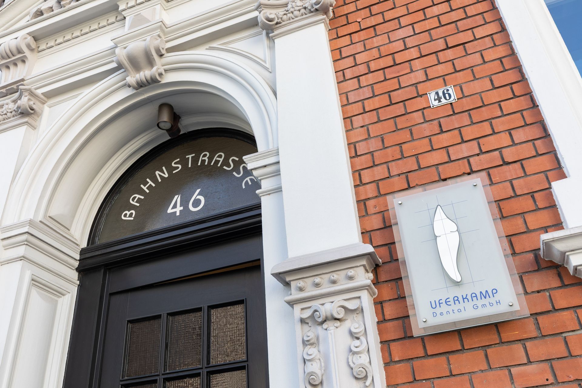 Ein Backsteingebäude mit einer schwarzen Tür ist von Bäumen und Blumen umgeben.