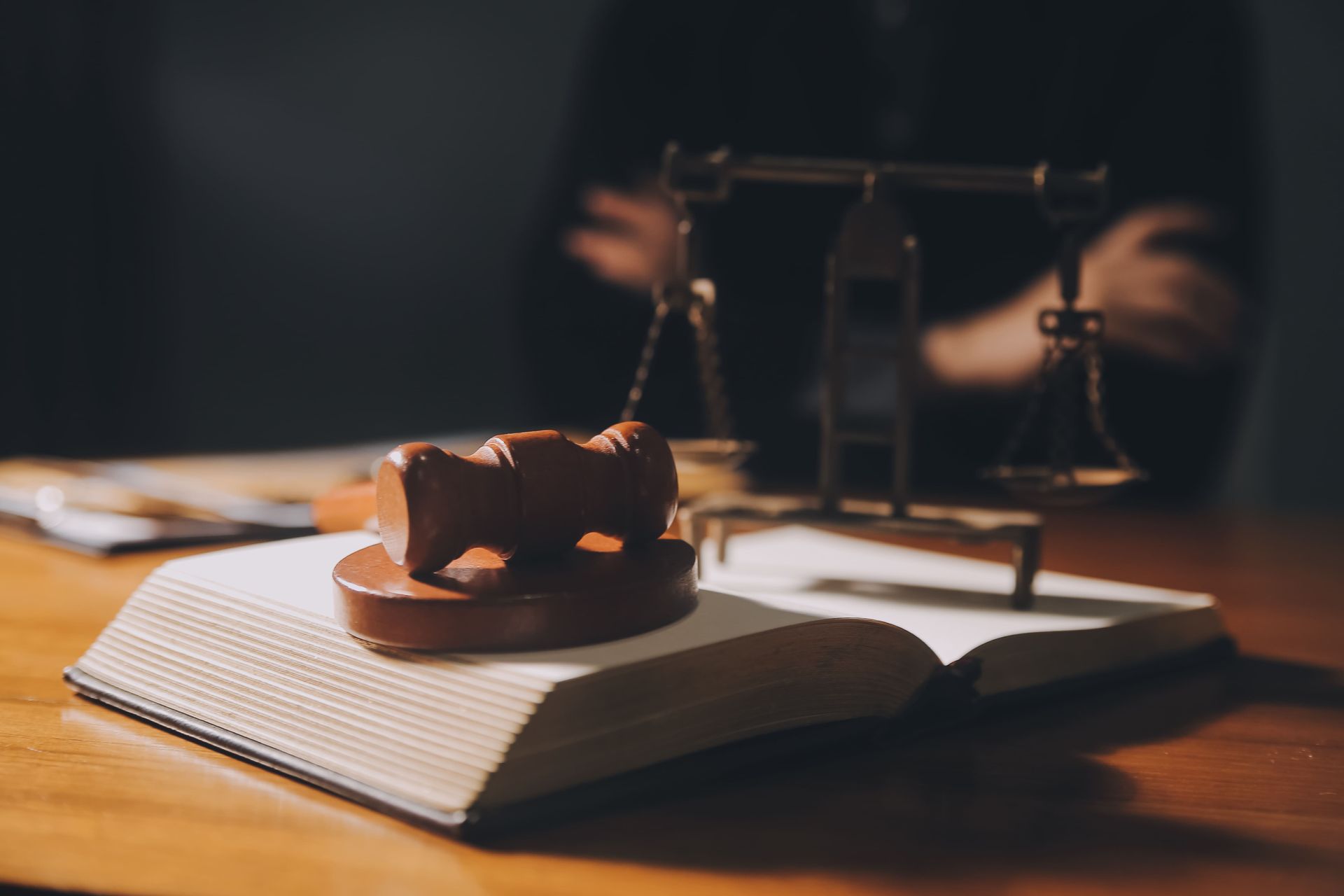 Un mazo sobre un libro abierto, con una balanza de la justicia al fondo, poco iluminada.