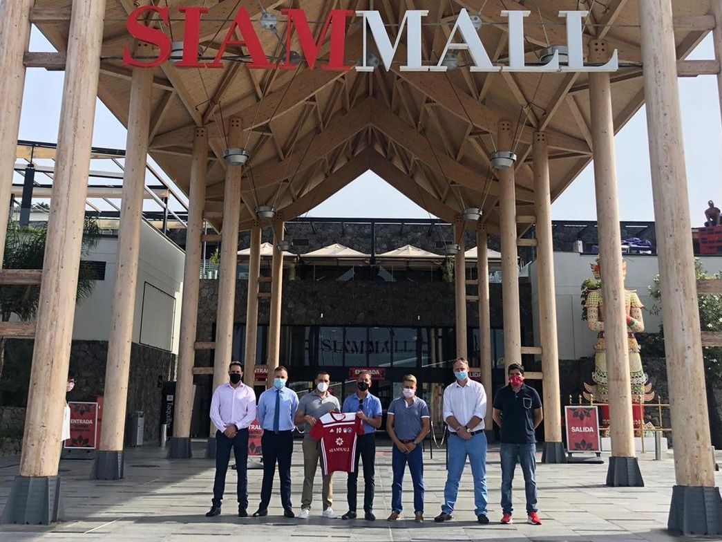 Un grupo de hombres se encuentra frente a la entrada del Siam Mall, sosteniendo una camiseta.