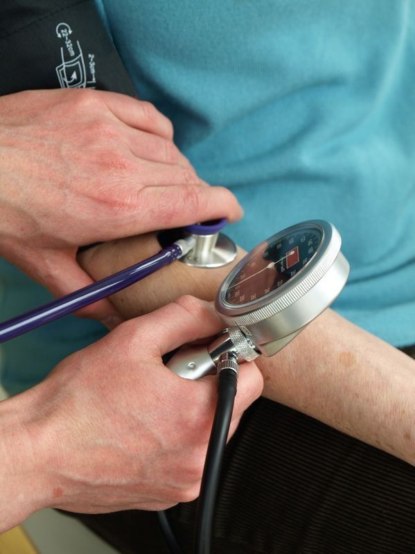 Médico tomando la presión arterial del paciente con un estetoscopio y un manguito de presión arterial manual en el brazo.