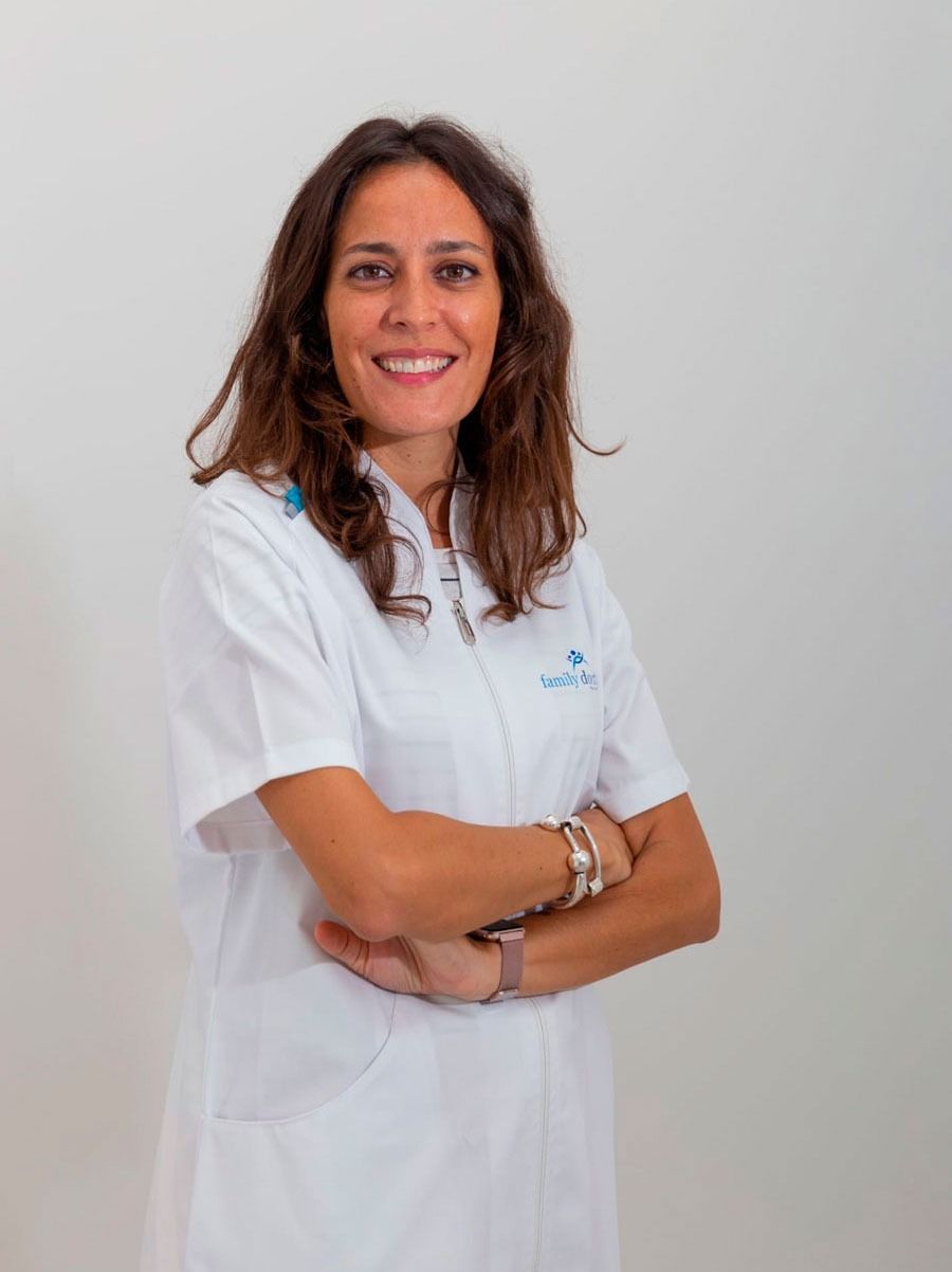 Mujer sonriente con una bata de laboratorio blanca y los brazos cruzados, en el interior.