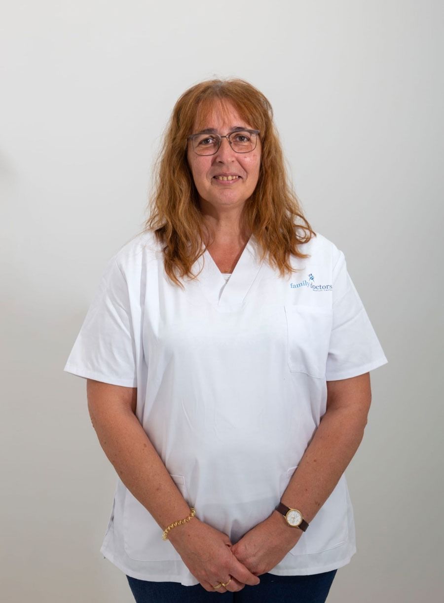 Mujer con gafas, con uniforme blanco, con los brazos cruzados y sonriendo sobre un fondo blanco.