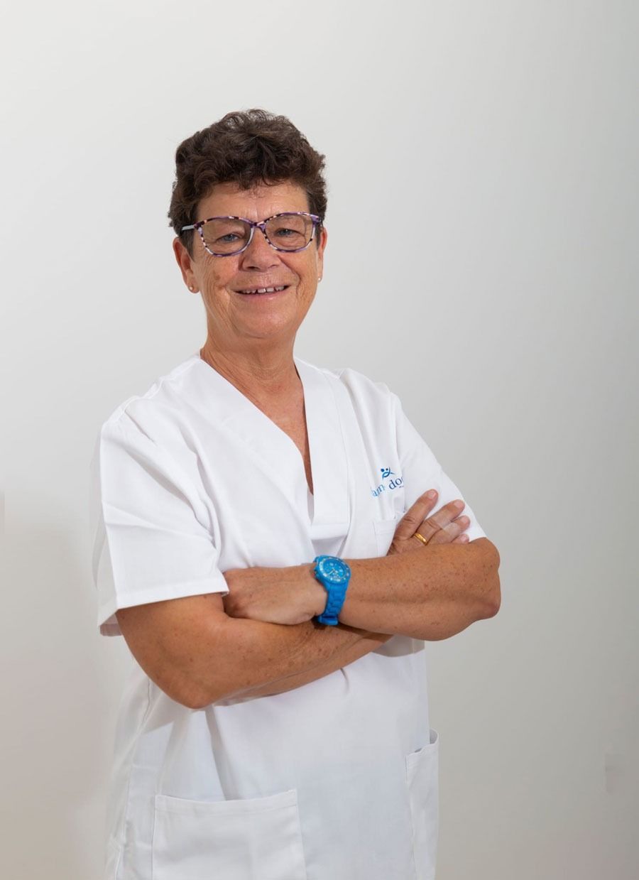 Mujer con uniforme blanco, gafas y reloj azul, con los brazos cruzados, sonriendo sobre un fondo blanco.