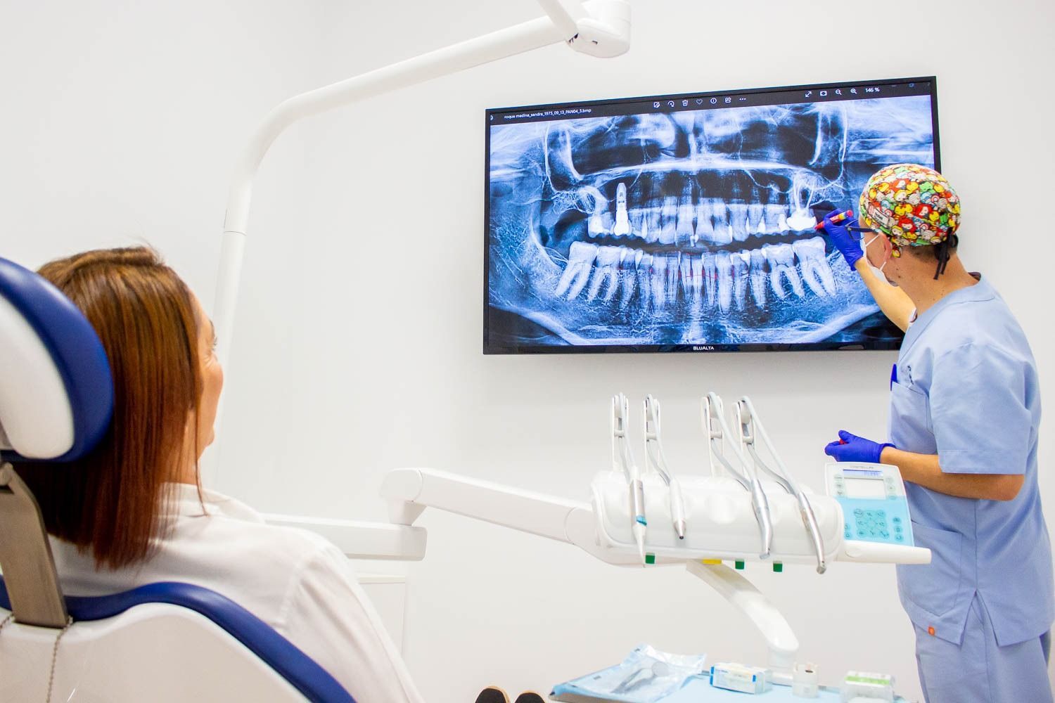 Dentista mostrando una radiografía dental a un paciente. En un entorno de oficina moderno y luminoso.
