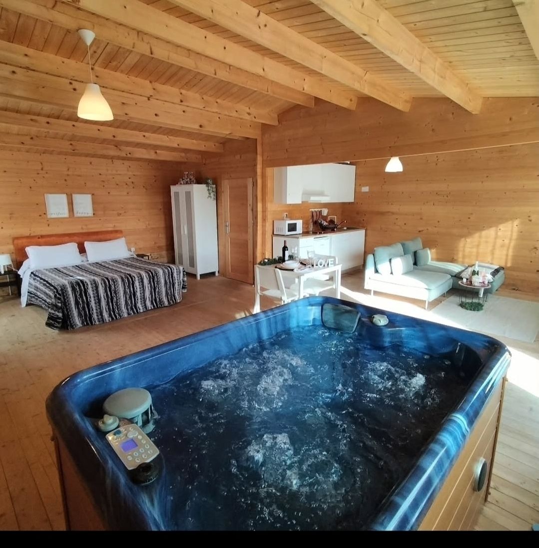 Jacuzzi en el interior de una cabaña revestida de madera, con cama, cocina y zona de estar visibles.