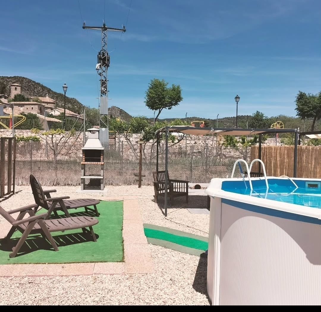 Patio trasero con piscina, camastros, parrilla y un pueblo de montaña al fondo.